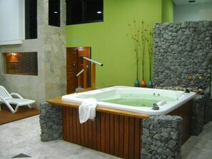 A spa area with a hot tub, stone walls, and a wooden bench. - Hotel Spa Brisolei (San Bernardo del Tuyú)