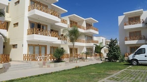 Un hotel moderno con varios pisos, balcones con barandillas de madera y un césped bien cuidado.