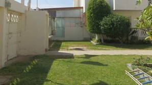 Un edificio residencial con fachada blanca, un balcón en el piso superior y un pequeño jardín delantero con césped y un árbol.