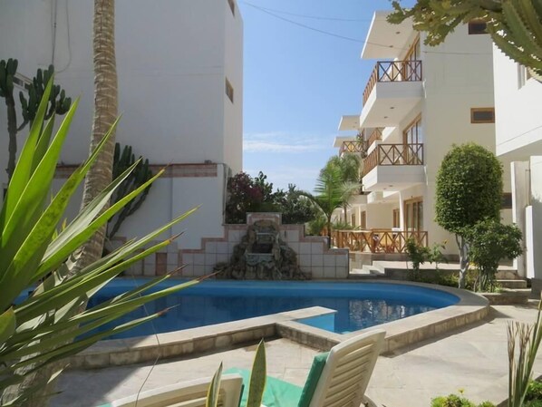 A pool area with a clear blue pool, surrounded by white buildings with balconies. - Hotel Emancipador (Ica)