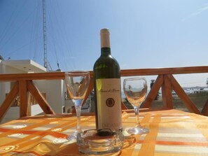 A bottle of Blanc de Blancos wine, two wine glasses, and a decanter on a table with a checkered tablecloth, overlooking a coastal view. - Hotel Emancipador (Ica)