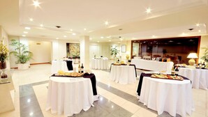 A spacious hotel lobby with multiple round tables set up for dining, each with white tablecloths and various food items.