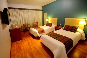 Habitación de hotel con dos camas, un escritorio con una computadora portátil, una silla y un televisor instalado en la pared.