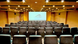 A conference room with rows of chairs, a large screen displaying 'HOTEL ARGOS', and a fire extinguisher on the wall.