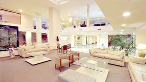 A spacious hotel lobby with a high ceiling, multiple seating areas, and a view of the upper floor.