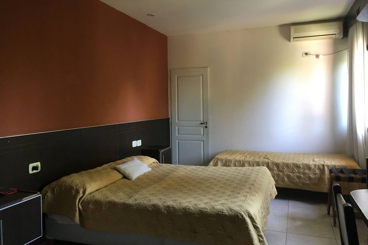 A hotel room with two beds, a door, an air conditioning unit, and a desk.
