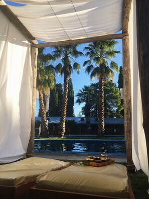 A tented outdoor seating area with a view of palm trees and a building in the background. - Hotel Puesta del Sol (San Rafael)