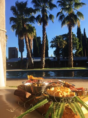 A dining table with various food items and a view of palm trees and a building in the background. - Hotel Puesta del Sol (San Rafael)