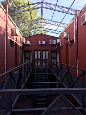 A covered walkway with metal railings leading to a building with multiple air conditioning units and windows with curtains. - Hotel Puesta del Sol (San Rafael)