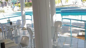 A pool area with white chairs and tables, a blue pool, and a tiled floor. - Hotel Miranda Cumberland  (Santa Ana)