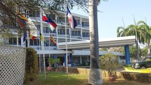 A hotel with multiple flags, a covered outdoor area, and a building with balconies. - Hotel Miranda Cumberland  (Santa Ana)