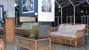 A lobby with wicker furniture, a glass coffee table, and framed artwork on the walls. - Hotel Miranda Cumberland  (Santa Ana)