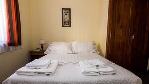 Una cama bien hecha con dos toallas dobladas, una lámpara de noche y un cuadro en la pared.