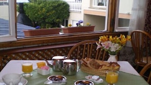 Un desayuno con una mesa para dos, que incluye platos, tazones, una cafetera, un hervidor de té, una cesta de pan y un florero con flores.