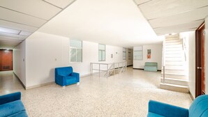 Una habitación amplia con techo alto, un sillón azul, una mesita y una escalera que conduce a otro nivel.