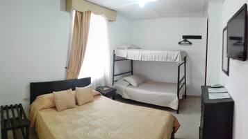 Un dormitorio con una cama individual, una cama litera, un escritorio con silla, un radiador y un televisor en la pared.