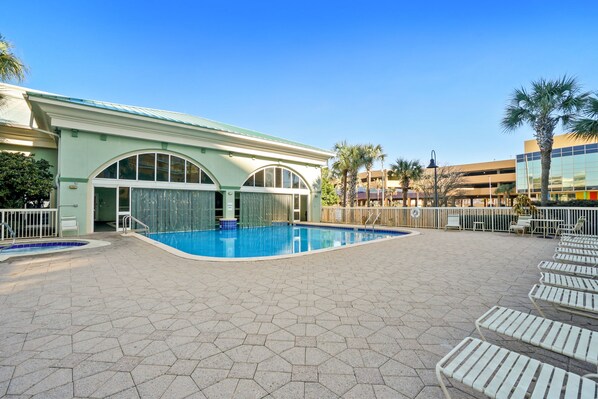 A swimming pool area with hexagonal tiles, lounge chairs, and a building with arched windows.