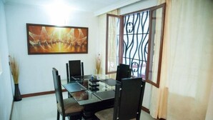 A dining area with a glass table, dark chairs, a painting on the wall, and a window with decorative metal bars. - Apartamento Viscaya (Medellin)