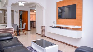 A modern living room with a flat-screen TV mounted on a wooden panel, a glass coffee table, and a black leather sofa. - Brown Stone Apartments (Medellín)