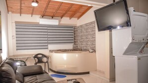 A modern living room with a leather sofa, a coffee table, a TV, a built-in bathtub, and a washing machine. - Brown Stone Apartments (Medellín)