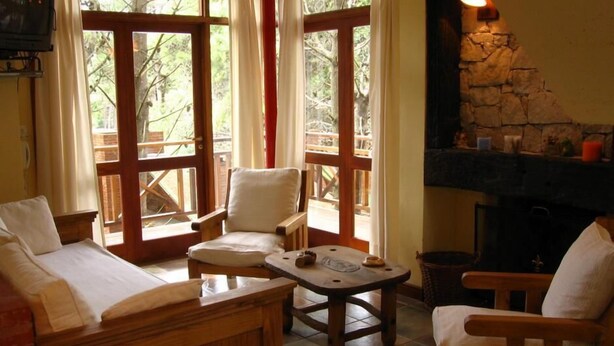 A cozy room with a wooden sofa, a chair, a small table, and a stone fireplace. - Le Cuyen Aparts (Mar de Las Pampas)