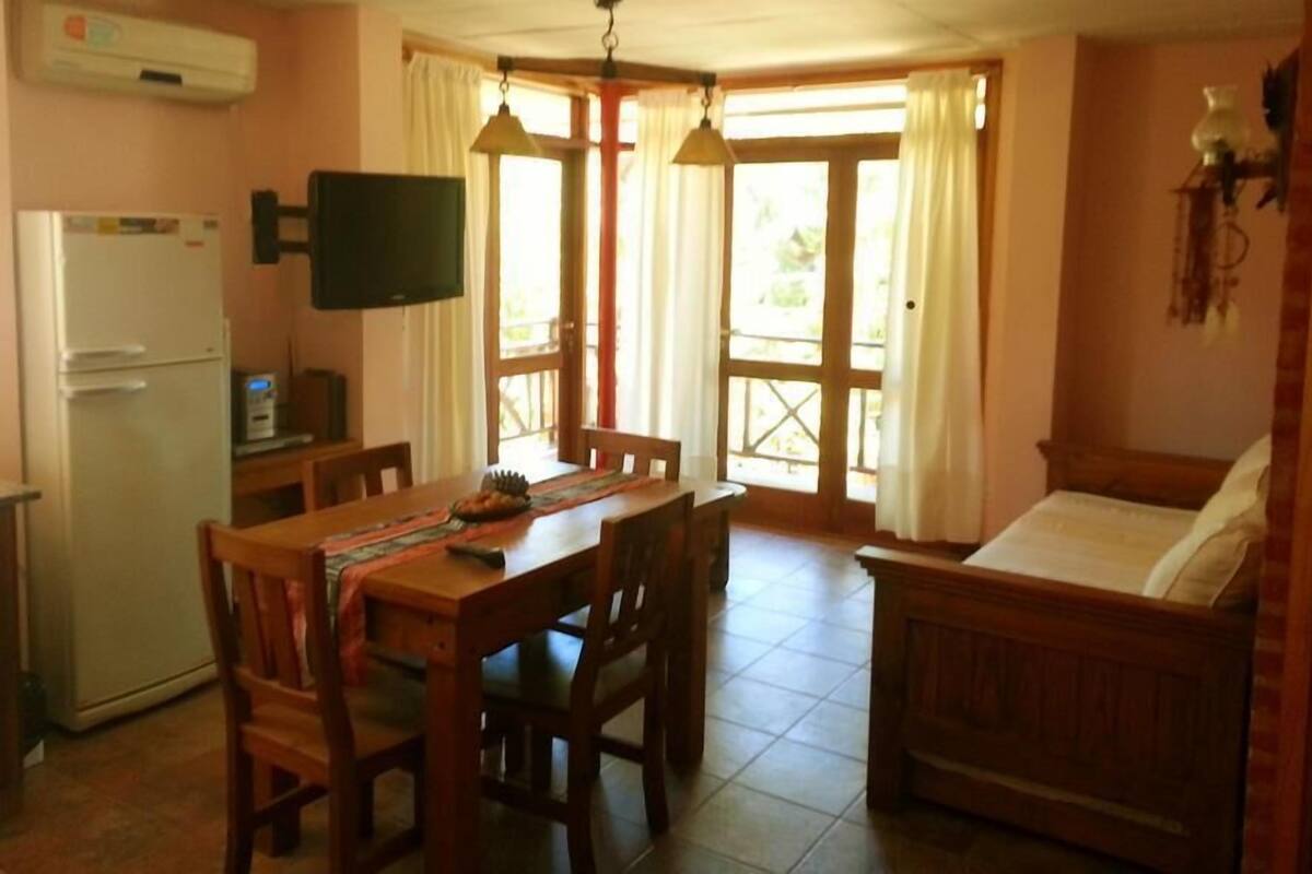A compact kitchen with a dining table, chairs, a sofa, and a TV.
