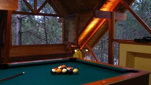 A pool table with balls in a room with wooden beams and large windows overlooking a forest. - Le Cuyen Aparts (Mar de Las Pampas)