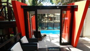 A covered outdoor seating area with wicker furniture and a glass table, overlooking a swimming pool. - Le Cuyen Aparts (Mar de Las Pampas)