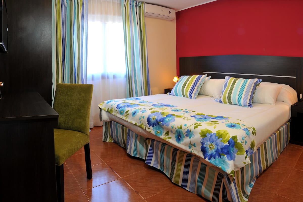Ein Hotelzimmer mit Bett, Stuhl, Schreibtisch und Nachttisch mit Lampe.
