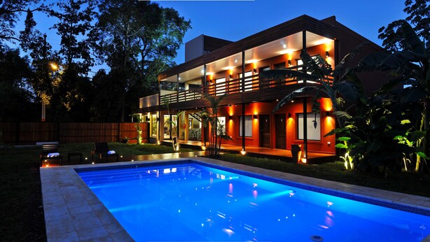 A modern two-story house with a swimming pool, surrounded by a wooden fence and tropical plants. - Costa Iguazú Apart Hotel (Puerto Iguazú)