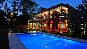 A modern two-story house with a swimming pool, surrounded by a wooden fence and tropical plants. - Costa Iguazú Apart Hotel (Puerto Iguazú)