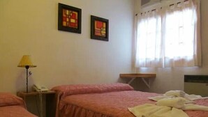 A hotel room with two beds, a bedside table with a lamp, and a window with curtains.