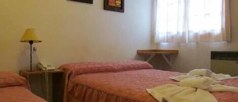 Habitación de hotel con dos camas, una mesita de noche con lámpara y una ventana con cortinas.