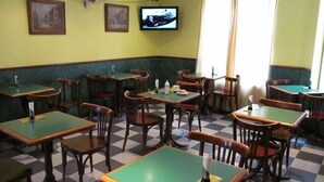 A restaurant with green tables and chairs, checkered floor, and a television on the wall.
