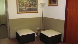 A room with two black ottomans, a floor lamp, and two framed pictures on the wall.