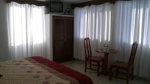 A hotel room with a bed, a TV, a wardrobe, and a small table with chairs.