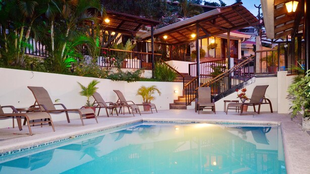 Ein Pool mit Liegestühlen, eine Treppe und eine überdachte Terrasse mit Pflanzen und Beleuchtung.