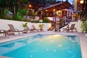 A swimming pool with lounge chairs, a staircase, and a covered patio area with plants and lighting. - Casa Reflejos Apartamento 8 (Escazu)
