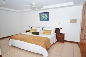 A neatly arranged bedroom with a bed, bedside tables, a ceiling fan, and a painting on the wall. - Casa Reflejos Apartamento 8 (Escazu)