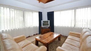 Ein Wohnzimmer mit Holzbalkendecke, einem Fernseher auf einem Schrank und beigefarbenen Sofas.