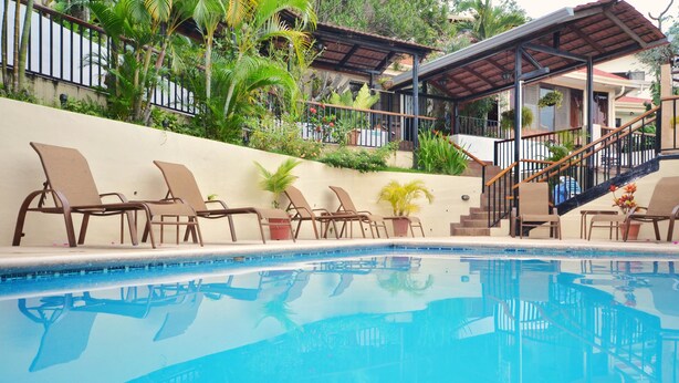 Zona de piscina con sillones de descanso y un espacio de estar cubierto.