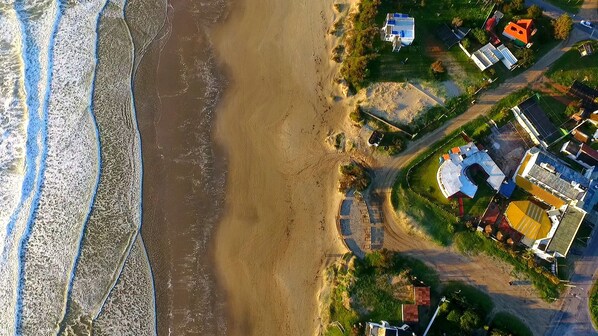 An aerial view of a coastal area with a beach, houses, and a small marina.