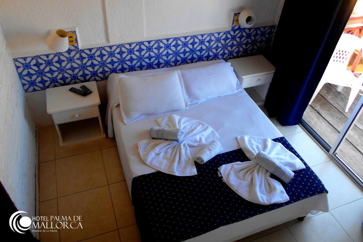 Habitación de hotel con cama, mesita de noche, espejo de baño y ventana.