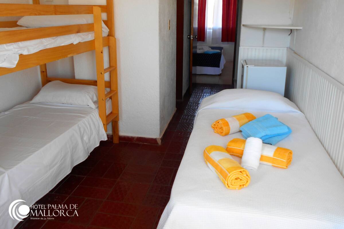 Habitación de hotel con dos camas individuales, una con cabecera de madera y la otra con cabecera blanca. Hay toallas sobre la cama y un radiador en la pared.