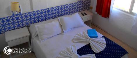 A hotel room with a bed, a nightstand, an air conditioning unit, a lamp, and a window with red curtains.