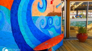 Une fresque colorée avec un motif ondulé, un panneau en forme de flèche rouge et une plante en pot, le tout sur une terrasse en bois.