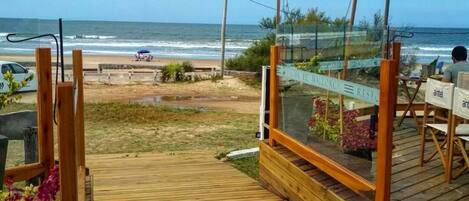 A wooden deck leading to a beachside restaurant with outdoor seating and a view of the ocean.