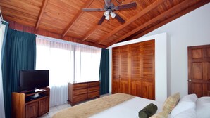 Une chambre à coucher avec un lit, une télévision, des meubles en bois et un ventilateur de plafond.