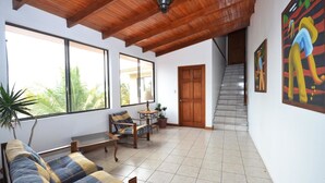 Un vaste espace de vie doté d’un plafond en bois, de grandes fenêtres, d’un canapé, d’une table et d’un escalier.