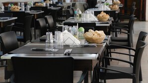 A restaurant with multiple tables, each set with clear glasses, napkins, and bread baskets.